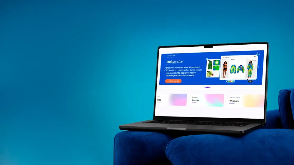 A laptop on a blue chair displays an Audaces webpage with a Looksmaker promotional banner and fashion images.
