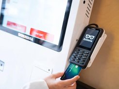 Close-up of a Kayana-branded card payment terminal mounted beside a kiosk, with a card held near the reader.