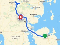 Mobile app map of Denmark showing a blue travel route between a green point near Odense and a red stop marker, with navigation tabs at the bottom.