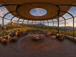 Wide panoramic view inside a glass observatory overlooking mountains at sunset.