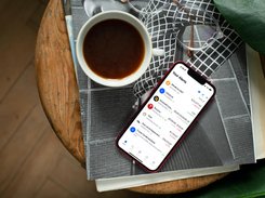A phone on a table beside coffee and reading glasses displays the Stock Alarm alerts list.