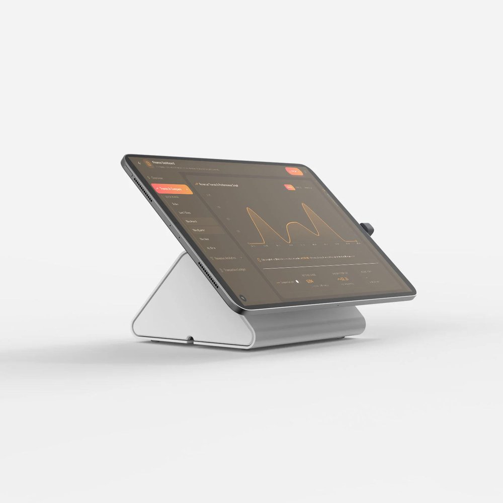 A tablet mounted on a white angled stand displays a dark dashboard with a left navigation panel, orange controls, a line chart, and summary metrics.