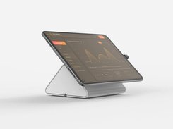 A tablet mounted on a white angled stand displays a dark dashboard with a left navigation panel, orange controls, a line chart, and summary metrics.