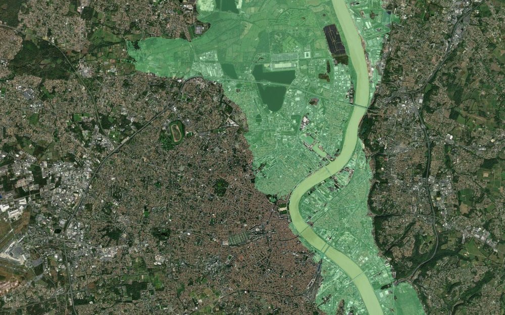 Satellite image of a city and river with a translucent green polygon overlay covering the riverside area.
