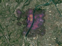 Satellite image of a dense city beside a river with a multicolored heatmap-like overlay concentrated in the urban center.