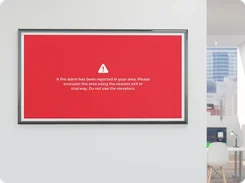 Wall-mounted digital display shows a red fire alarm evacuation alert message.