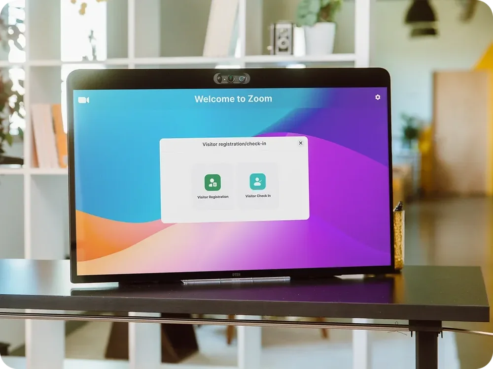 A desk-mounted display shows a Zoom welcome screen with a visitor registration/check-in dialog offering Visitor Registration and Visitor Check In.